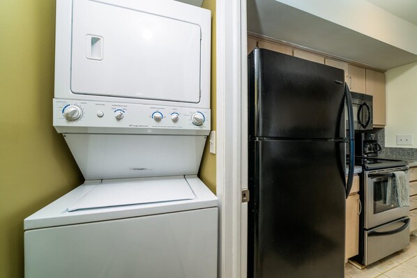 Una cocina compacta con lavadora y secadora blancos, un refrigerador negro y una estufa.