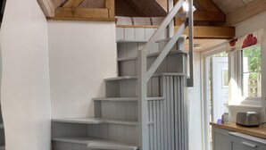 A staircase with a wooden finish, a white wall, and a kitchen area with a toaster and a window. - Cozy cabin in nature! A great base to relax or explore North Norfolk . (Norfolk)