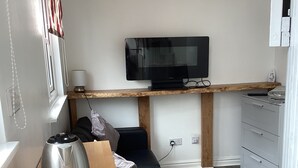 A compact living space with a kitchenette, a black sofa, a wooden table, a coffee maker, and a TV mounted on a wooden shelf. - Cozy cabin in nature! A great base to relax or explore North Norfolk . (Norfolk)
