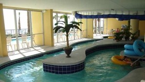 An indoor swimming pool with a tiled edge, a small island with a plant, and lounge chairs around the pool area. - 25 ft. Balcony Oceanfront ! Incredible views !MONTHLY WINTER RENTAL AVAILABLE ! (Myrtle Beach)