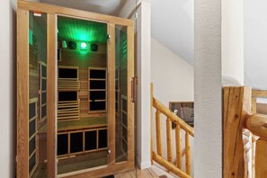 A wooden sauna with glass doors, a wooden staircase, and a white wall.