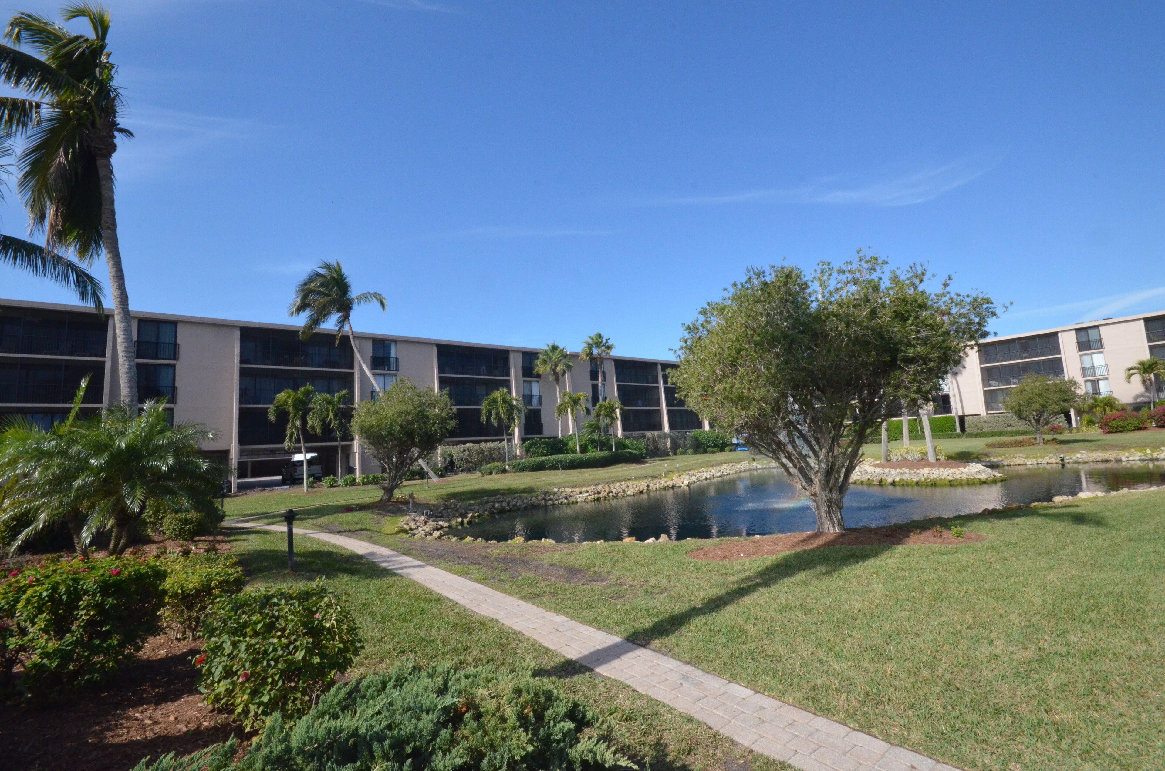 A modern building with a paved walkway, a small pond, and palm trees.
