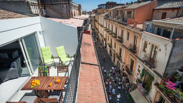 A narrow street with buildings on either side, a balcony with a table and chairs, and a view of the street below. - Splendid apartment with terrace overlooking Corso Umberto, Taormina, Sycily (Taormina)