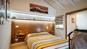 A bedroom with a wooden headboard, a colorful striped bedspread, a nightstand with a lamp, and a painting above the bed. - Splendid apartment with terrace overlooking Corso Umberto, Taormina, Sycily (Taormina)