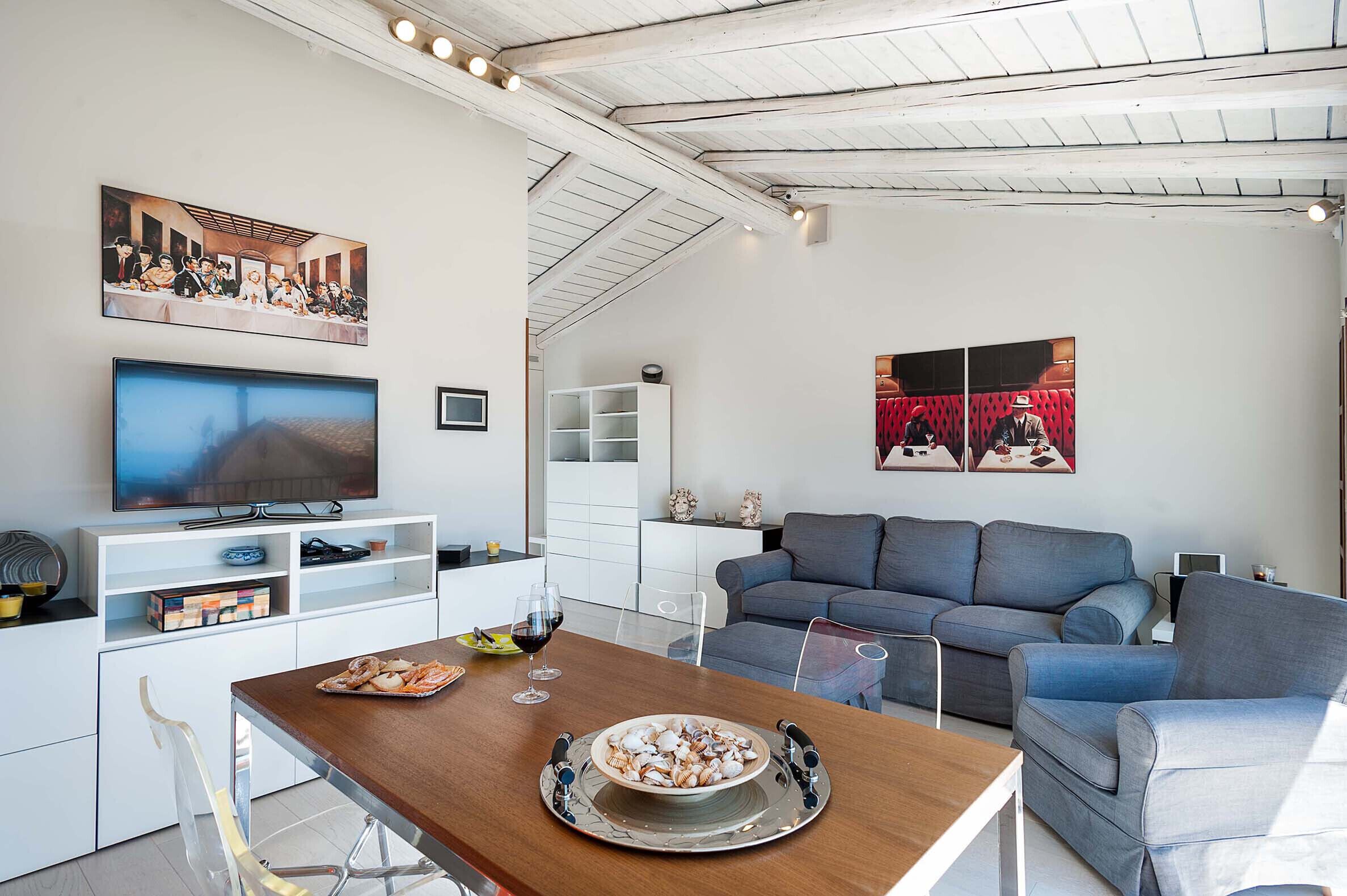 A modern living room with a dining area, a television, and artwork on the walls.
