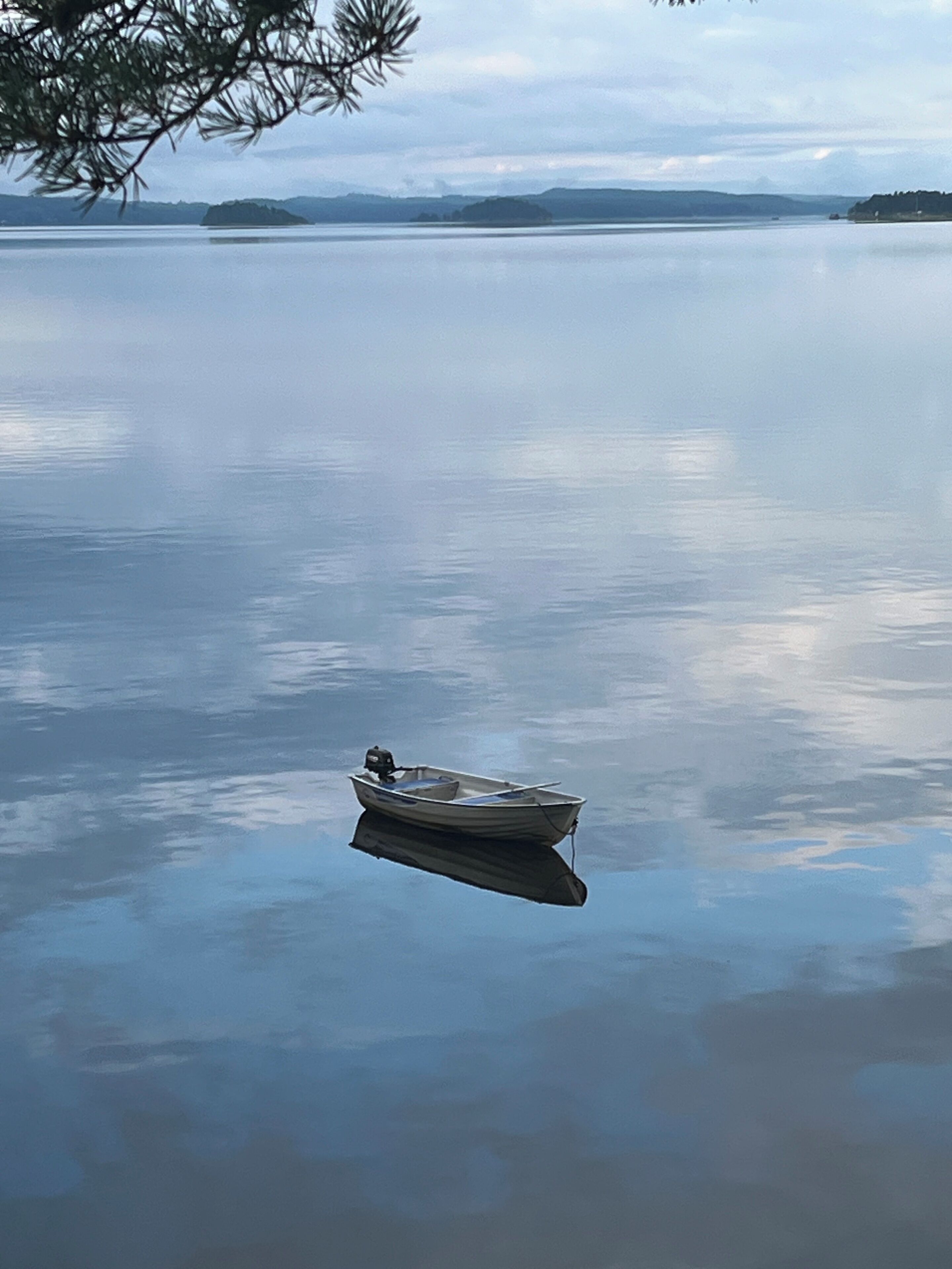 A small boat anchored on a calm lake with distant landforms.