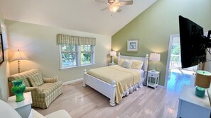 A bedroom with a bed, two nightstands, a television, a window with blinds, and a ceiling fan.