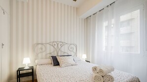 A neatly made bed with floral bedding, two bedside lamps, and rolled towels on the bed.