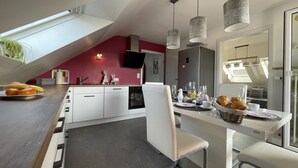 A modern kitchen with white cabinets, a dining area with a white chair, and a breakfast setup including bread and fruit. - Modern apartment in Schauenstein with loggia and balcony **** (Schauenstein)