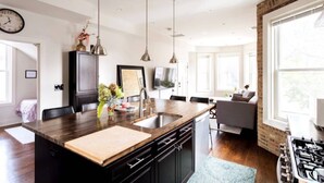 Una cocina moderna con una isla central, armarios negros, electrodomésticos de acero inoxidable, iluminación colgante y un amplio ventanal que proporciona luz natural.