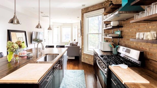 Una cocina moderna con una isla central, electrodomésticos de acero inoxidable y una pared decorativa de ladrillo.