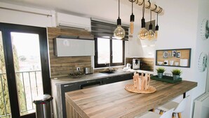 A modern kitchen with a wooden island, white bar stools, hanging pendant lights, and a view through a sliding door. - Apartment for 6 people, air-conditioned, with a view of the port at the Marines de Cogolin (COGOLIN)
