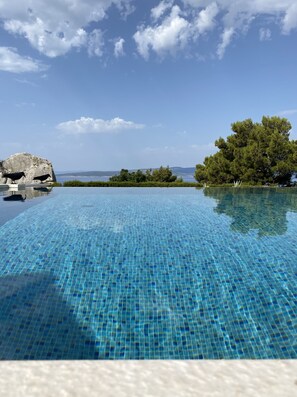 En vacker, turkosblå infinitypool med utsikt över havet och träden.