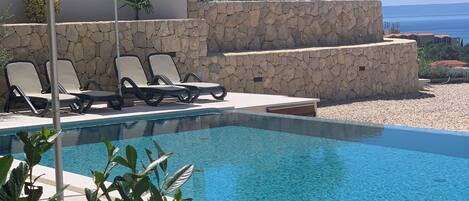 A pool with lounge chairs and an umbrella, surrounded by stone walls and greenery.
