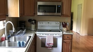Une cuisine avec des meubles de rangement en bois, un four à micro-ondes en acier inoxydable, une cuisinière blanche et un évier.