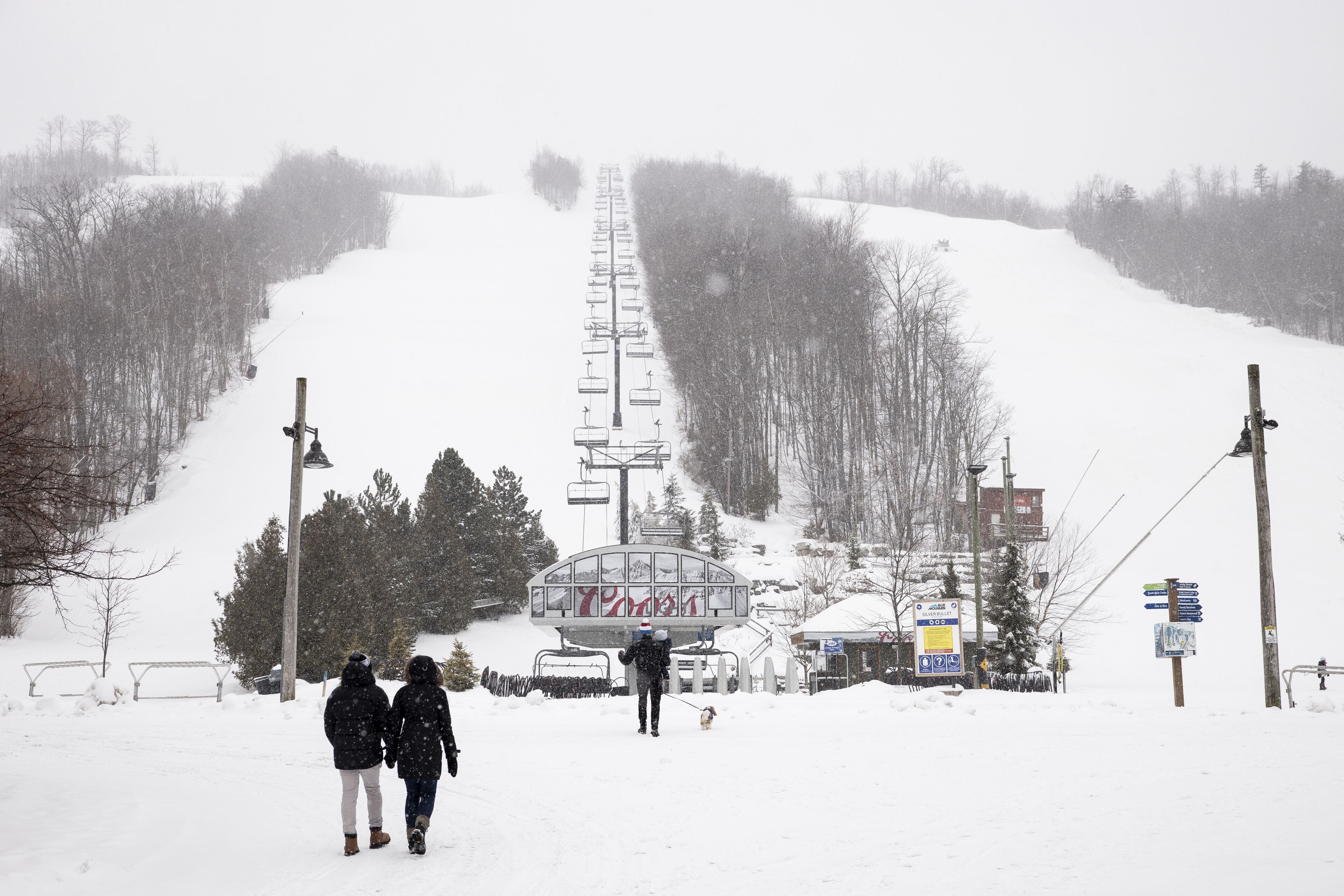 A snow-covered ski lift with people walking towards it.