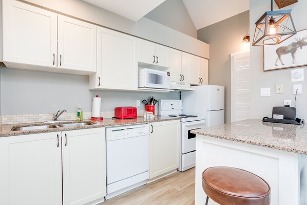 A modern kitchen with white cabinets, a granite countertop, a microwave, a toaster, and a refrigerator. - Great location! Spacious 2 bedroom Chalet at Blue! (The Blue Mountains)