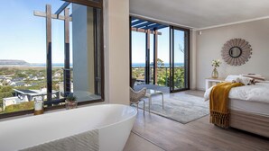 Ein modernes Schlafzimmer mit einer großen Badewanne, Meerblick und einem Balkon mit einer Holzpergola.