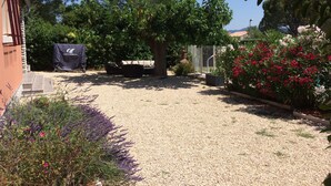 Un jardin avec un chemin de gravier, un espace de repos abrité et diverses plantes.