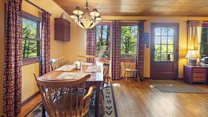 A dining area with a wooden table, chairs, and a chandelier. There are windows with curtains, a door, and a small cabinet. - Cabin near BR/Boone, fire pit, WIFI, secluded, nearby hikes, and VIEWS!! (Blowing Rock)