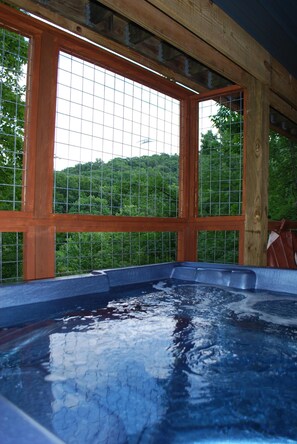 Un jacuzzi con estructura de madera y grandes ventanales, que ofrece vistas a una colina boscosa.