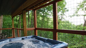 Un jacuzzi con una terraza de madera y grandes ventanales con vistas a un bosque.