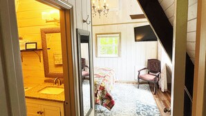 Un dormitorio en el ático con suelo de madera, una cama, una silla y una araña.