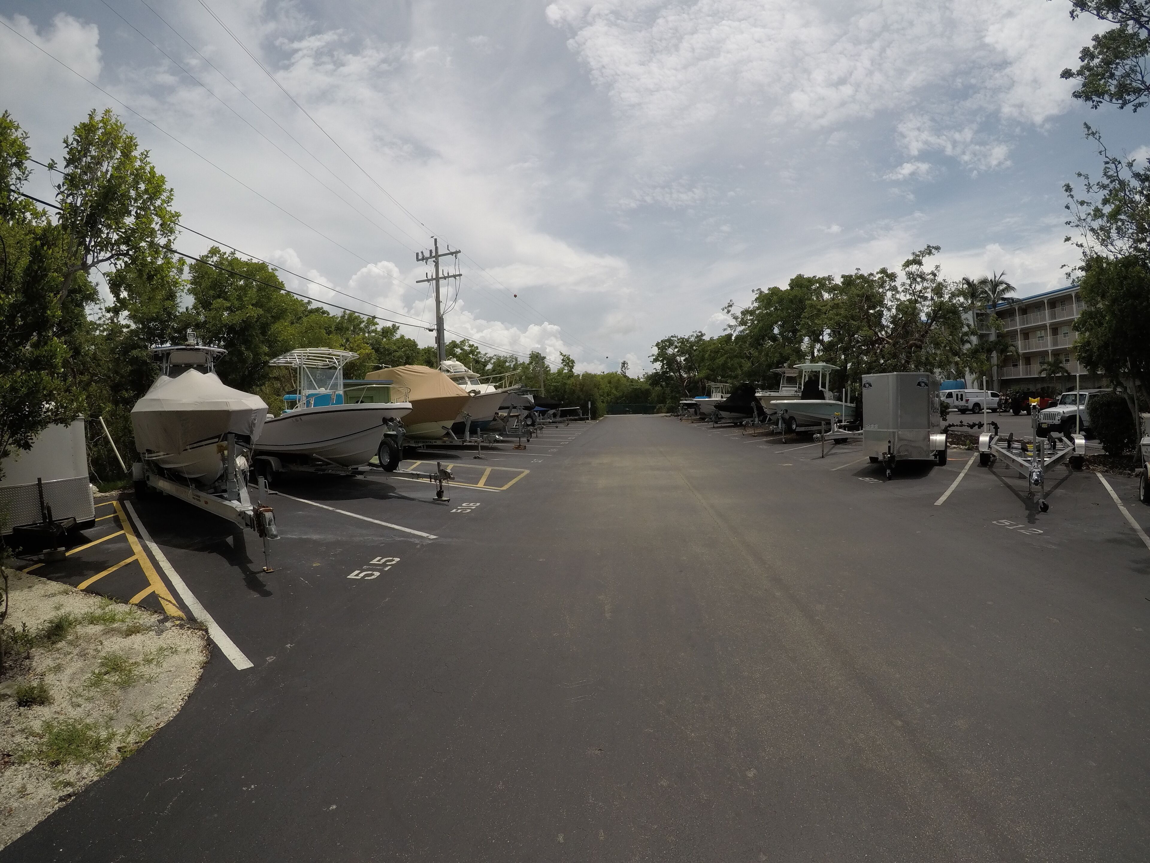 A parking lot with boats and trailers, surrounded by trees and buildings.