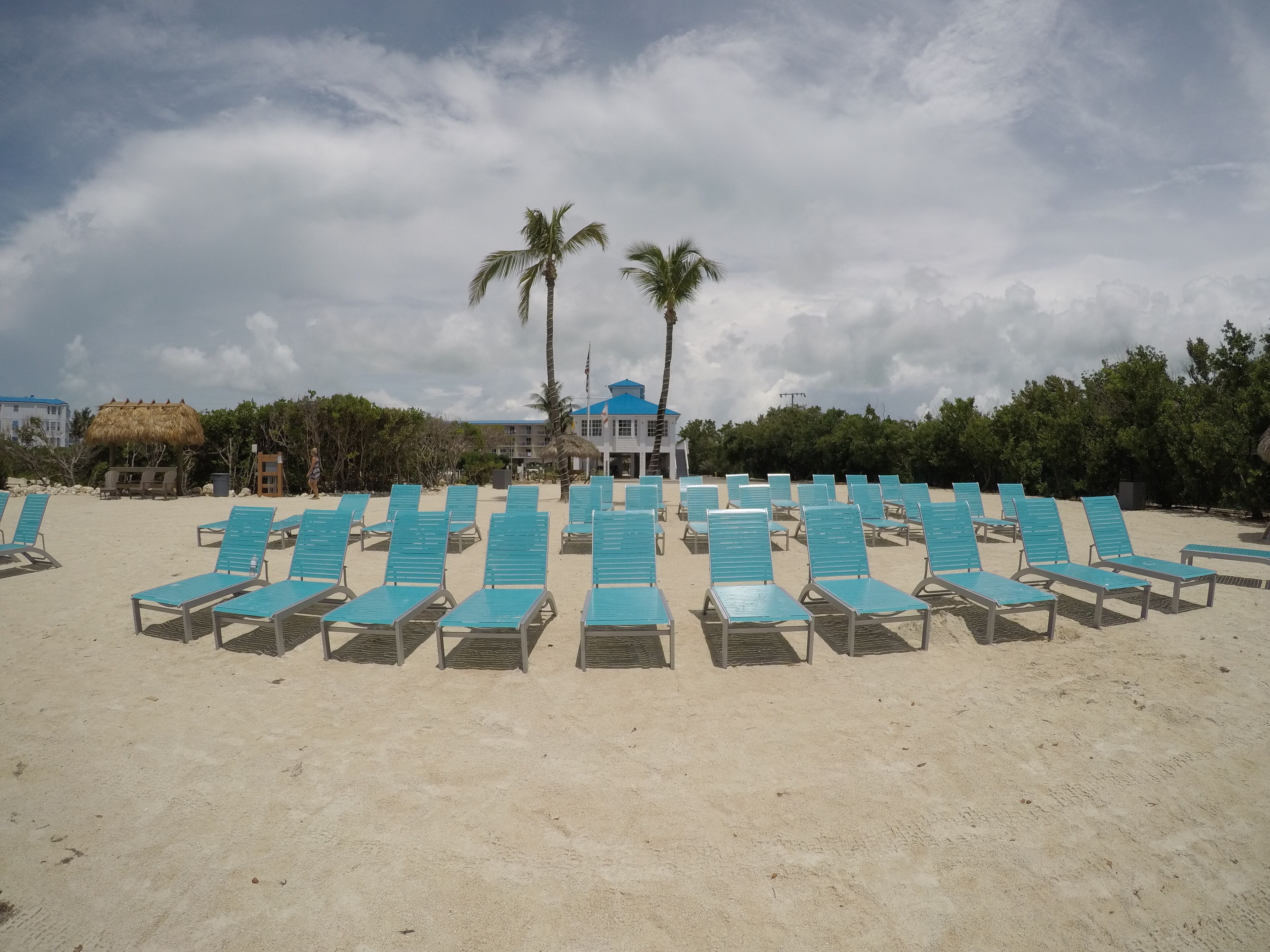 Ein Strand mit Reihen blauer Liegestühle und ein Gebäude mit blauem Dach im Hintergrund.