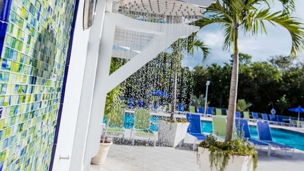 A modern showerhead with multiple water streams, a tiled wall, and a pool area with blue chairs and a palm tree. - Ocean view condo with balcony/marina view (Tavernier)