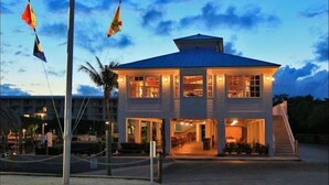 A two-story building with a flat roof, large windows, and a flagpole with multiple flags. - Ocean view condo with balcony/marina view (Tavernier)