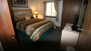 A bedroom with a bed, a bedside table with a lamp, a window with curtains, a door, and a framed picture on the wall.