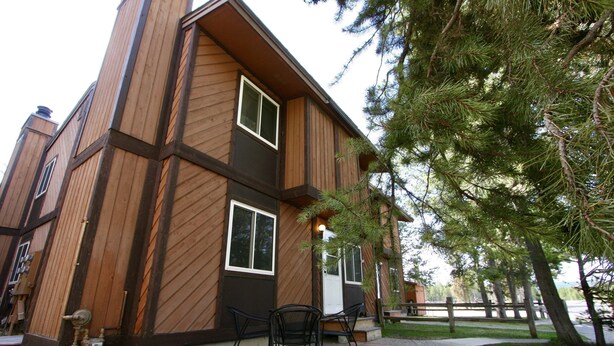 A modern two-story building with a wooden exterior and large windows. There is a patio area with outdoor seating.
