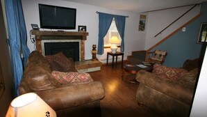 A living room with a fireplace, a television mounted above it, and two sofas with patterned cushions.