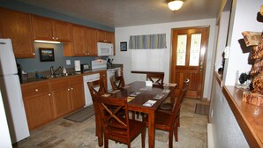 A kitchen with wooden cabinets, a dining table with chairs, a microwave, and a refrigerator.
