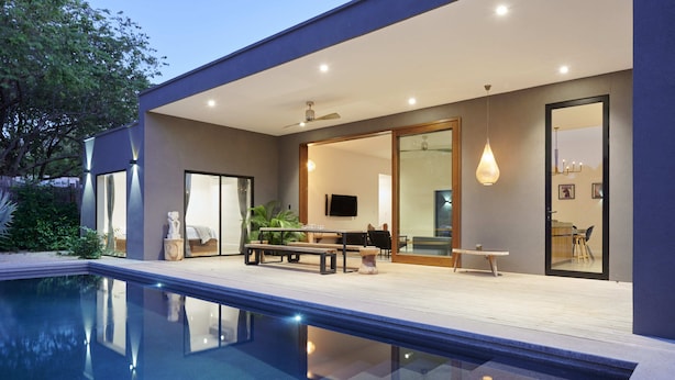 Ein modernes Haus mit Swimmingpool, einer Terrasse und Gartenmöbeln sowie einer großen Glaswand, die zu einem Innenbereich führt.