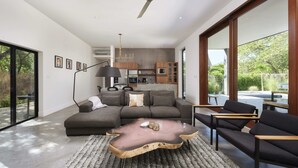Ein modernes Wohnzimmer mit einem Ecksofa, einem einzigartigen Holztisch und Blick auf die Küche und den Außenbereich.