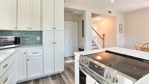 Una cocina moderna con armarios blancos, microondas integrado, estufa de acero inoxidable y una mesa de comedor de madera.
