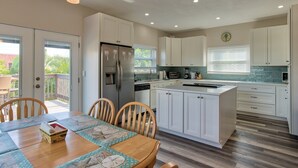 Una cocina moderna con armarios blancos, un refrigerador de acero inoxidable y un comedor con mesa y sillas de madera.