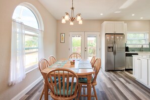 Un coin repas avec une table et des chaises en bois, un lustre, un réfrigérateur et une cuisine dotée de meubles blancs.