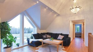 A spacious living room with a large window, a black sofa, a wooden coffee table, and a chandelier. - Beautiful home in Aneby with WiFi (Aneby)