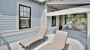 A covered deck with two lounge chairs and a wooden door. - Luxury Living Awaits: 5-Bed Retreat with Pool, Bikes, and Golf Cart in WaterColor! (Santa Rosa Beach)