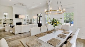 A spacious living room with a large dining table, white sofas, and a chandelier. - Luxury Living Awaits: 5-Bed Retreat with Pool, Bikes, and Golf Cart in WaterColor! (Santa Rosa Beach)