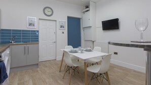 A modern kitchen with white cabinets, a blue door, a clock, and a dining area with a white table and chairs. - Townhouse Plus @ 40 West St (Crewe)