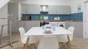 A modern kitchen with white cabinets, a dining table with chairs, and a small bar area. - Townhouse Plus @ 40 West St (Crewe)