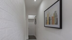 A hallway with white brick walls, a framed cityscape artwork, and a door at the end. - Townhouse Plus @ 40 West St (Crewe)