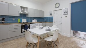 A modern kitchen with white cabinets, a blue tiled backsplash, a dining table with chairs, a clock, and a door with a number. - Townhouse Plus @ 40 West St (Crewe)