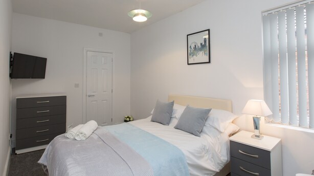 A bedroom with a bed, bedside table, lamp, and a TV mounted on the wall. - Townhouse Plus @ 40 West St (Crewe)