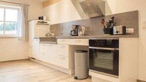 Een moderne keuken met een inbouwoven, een koffiezetapparaat en een prullenbak.