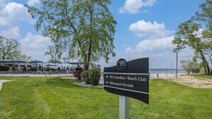 En skylt för Fin's Sandbar Beach Club och uthyrningen av vattensportutrustning, med utsikt över stranden och parasoller i bakgrunden.
